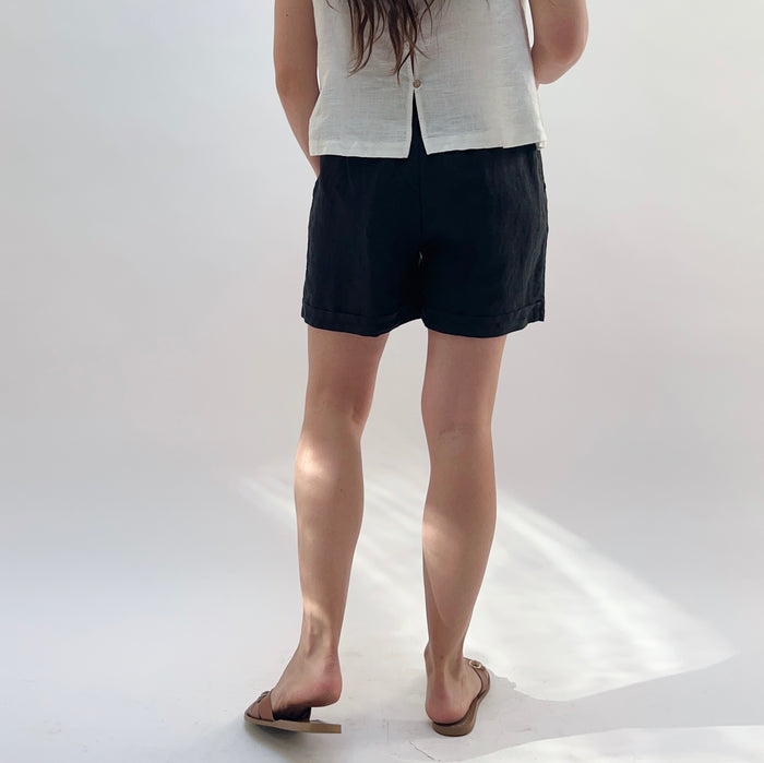 Person wearing black shorts and a white top on a plain background seen from behind