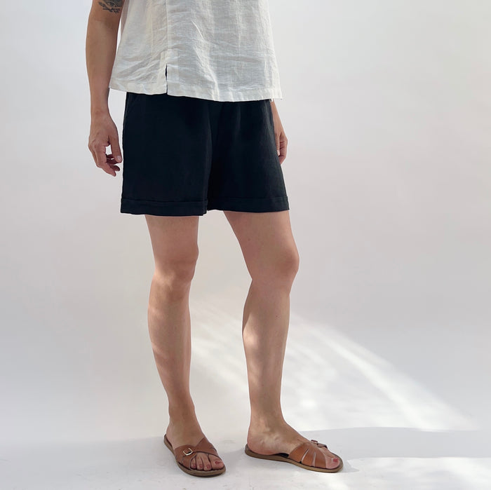 Person wearing black shorts and a white shirt on a plain background as seen from the side