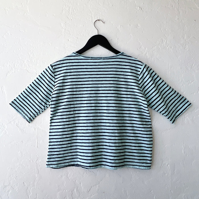 Blue and black striped shirt on a hanger against a white wall, viewed from behind