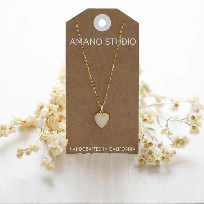 Beige locket displayed on an 'Amano Studio'-branded card with dried flowers surrounding