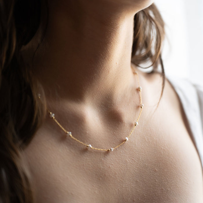 A person wearing a gold necklace with pearls interspersed along the chain.