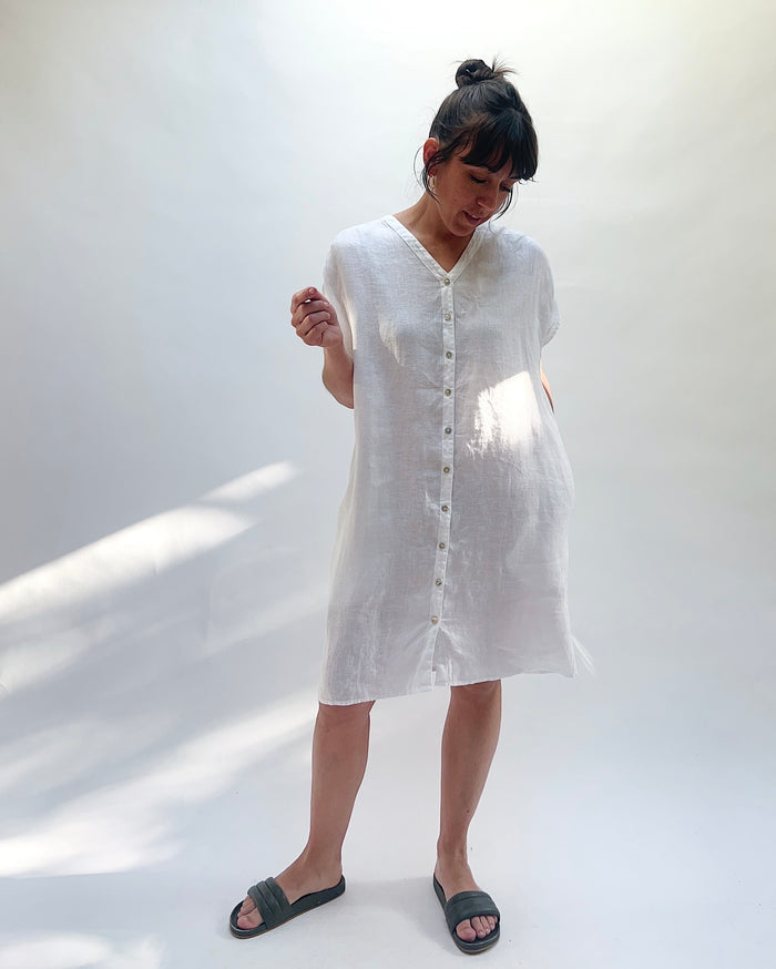 Woman wearing a white dress with buttons down the front against a white background