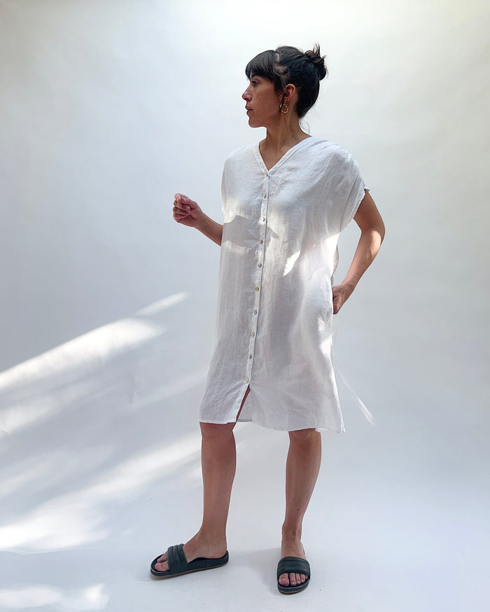 Woman wearing a white dress with buttons down the front against a white background