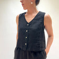 Person wearing a black sleeveless top with buttons on a plain background