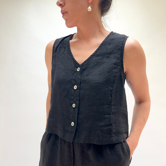Person wearing a black sleeveless top with buttons on a plain background