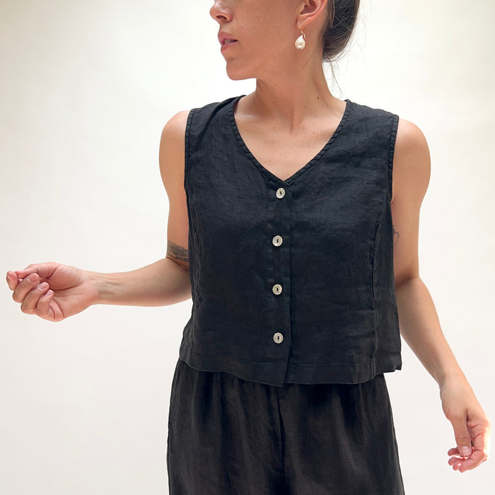 Person wearing a black sleeveless vest with buttons on a white background