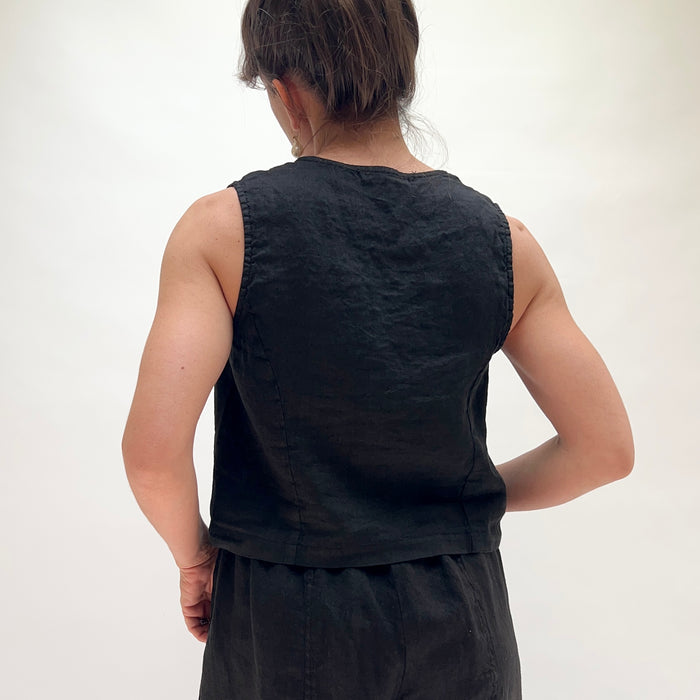 Person wearing a black sleeveless top and pants on a white background, viewed from the back