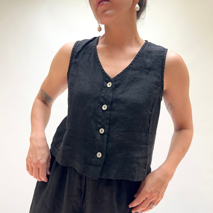 Person wearing a black sleeveless top with buttons on a plain background
