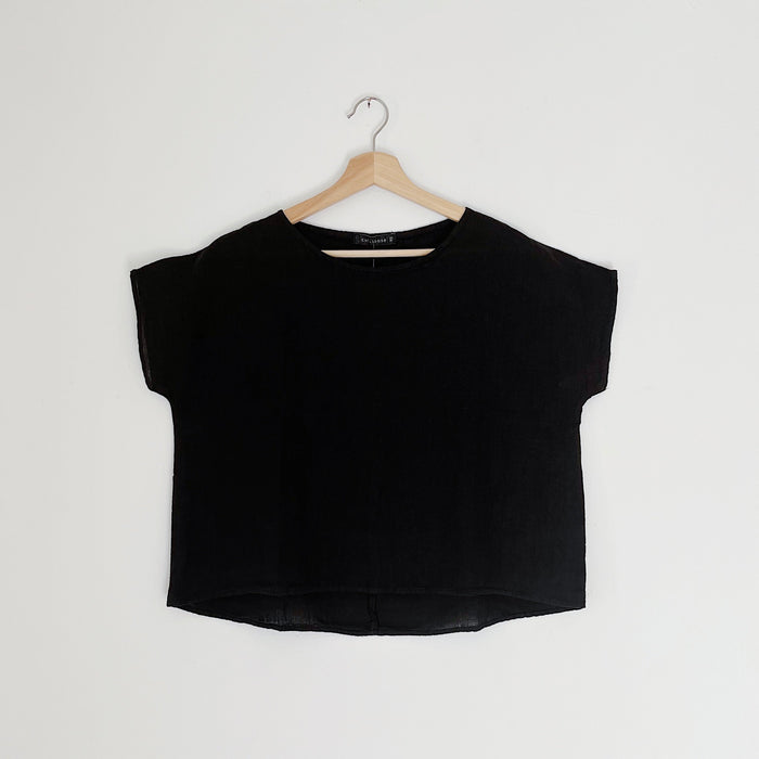 A black high-low hem linen tee shirt with a boat neckline, displayed on a wooden hanger against a white background.