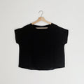 A black high-low hem linen tee shirt with a boat neckline, displayed on a wooden hanger against a white background.