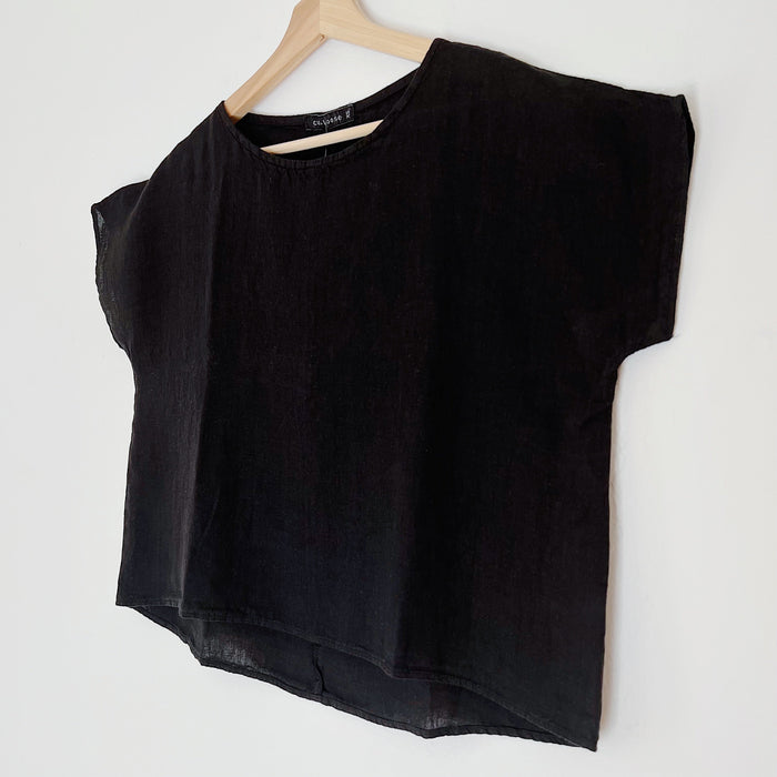 A black high-low hem linen tee shirt with a boat neckline, displayed on a wooden hanger against a white background, viewed from the side