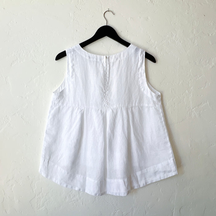 White linen high-low tank top by Cut Loose on a hanger, showing the relaxed A-line silhouette, scoop neck, and curved high-low hem as seen from behind