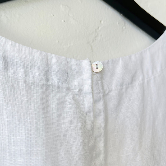 Close up detail of the button at the back of the neckline of the white linen high-low tank top by Cut Loose