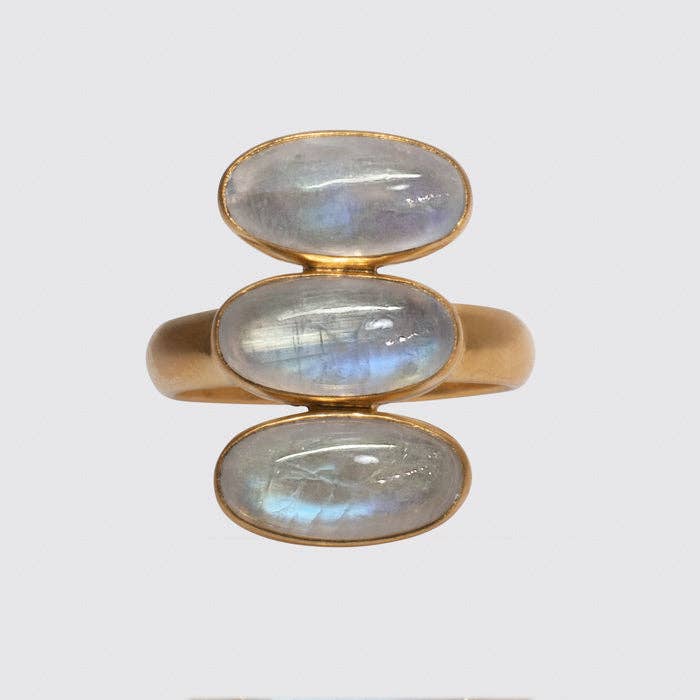 A gold-colored ring featuring three consecutive oval-shaped rainbow moonstone cabochons, bezel set with foil backing.