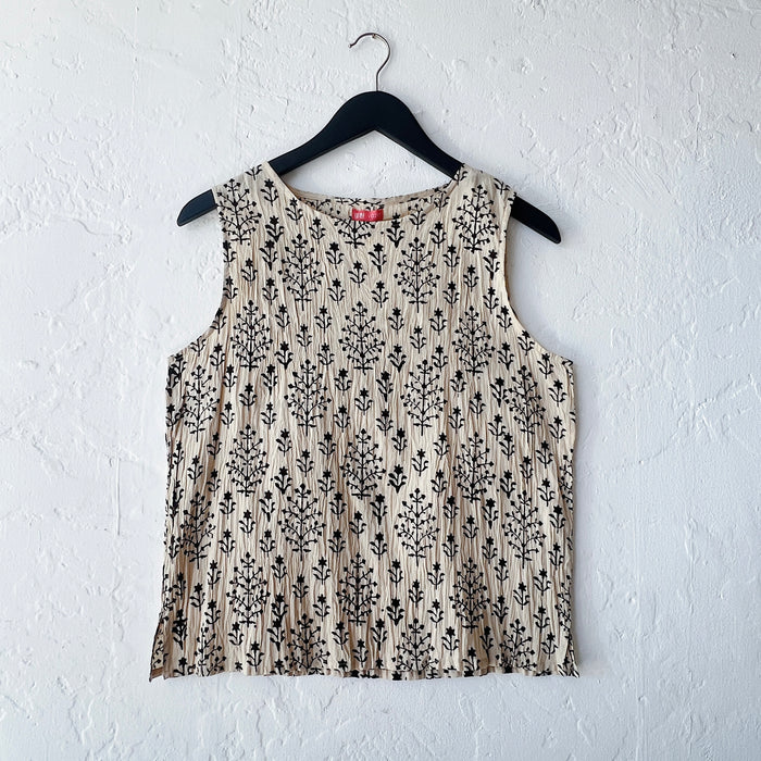 Beige sleeveless top with black floral pattern on a hanger against a white wall