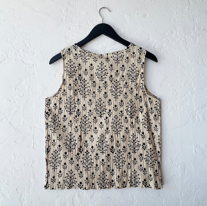 Beige sleeveless top with black floral pattern on a hanger against a white wall