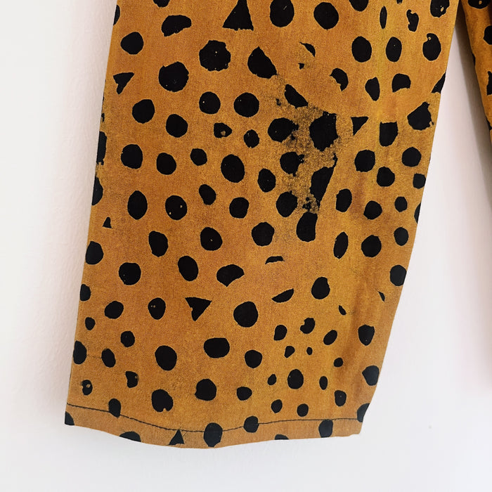 Close-up of the lower leg of the cheetah spot Batiki cotton kids pants, showing hand-printed black spots on golden amber cotton with natural hand-dye texture and hemline detail
