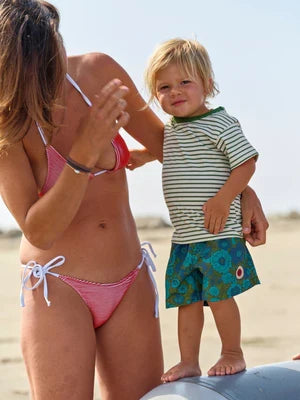 Woman in pink bikini and child in striped shirt and green shorts on a beach