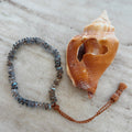 A faceted labradorite beaded bracelet with an adjustable tassel closure, displayed next to a conch shell on a textured background.