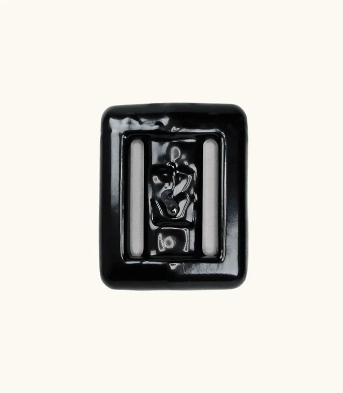 Close-up of a single black lava rock dive weight with glossy coating and two integrated belt slots, shown against a clean off-white background.