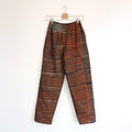 Lazy Pants in Persimmon Grid — full-length front view on hanger, loose-fit unisex pants in hand-dyed persimmon orange and black batik stripe print with elastic waist