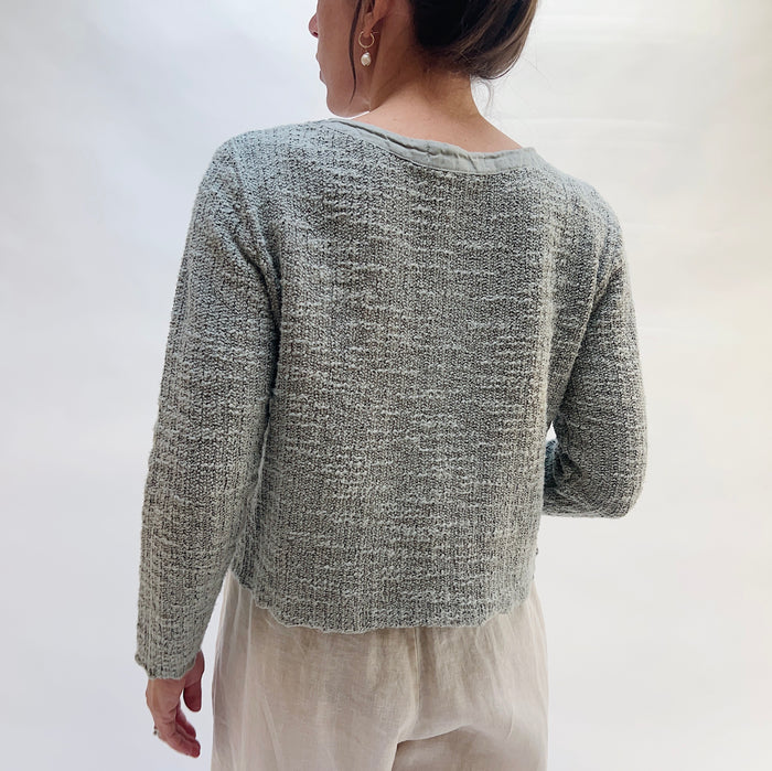 Person wearing a textured gray sweater against a white background, viewed from behind
