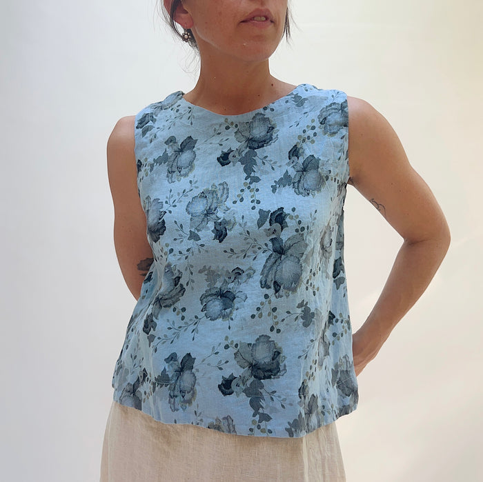 Woman wearing a sleeveless top with a floral pattern against a plain background