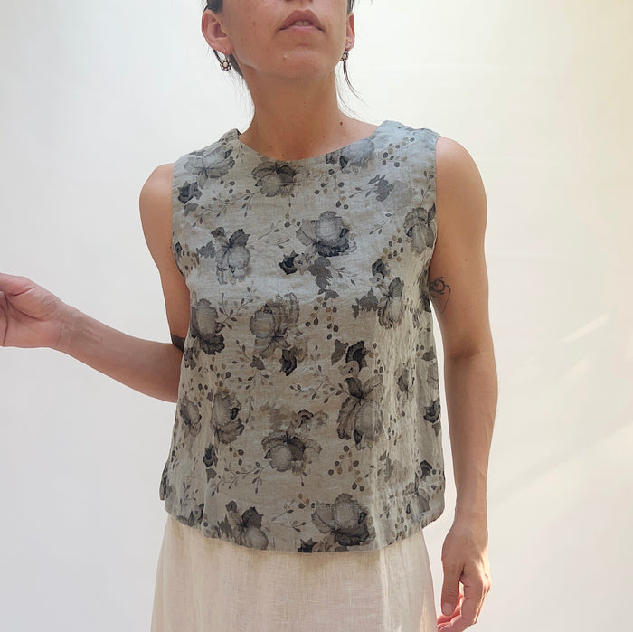 Woman wearing a sleeveless top with a floral pattern against a plain background