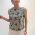 Woman wearing a sleeveless top with a floral pattern against a plain background