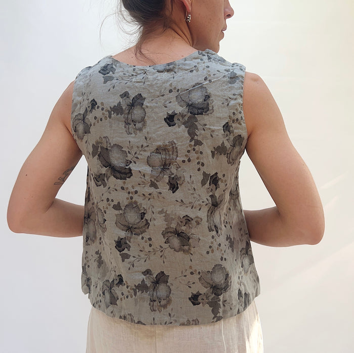 Person wearing a sleeveless top with floral pattern on a plain background, viewed from the back