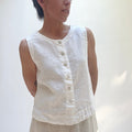 Person wearing a white sleeveless top against a plain background