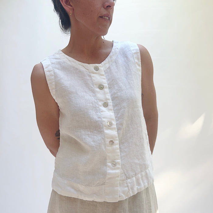 Person wearing a white sleeveless top against a plain background