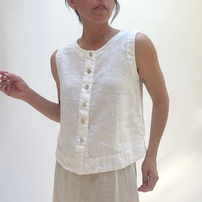 Woman wearing a white sleeveless top with buttons against a plain background