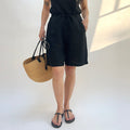Person wearing a black dress holding a woven bag on a white background