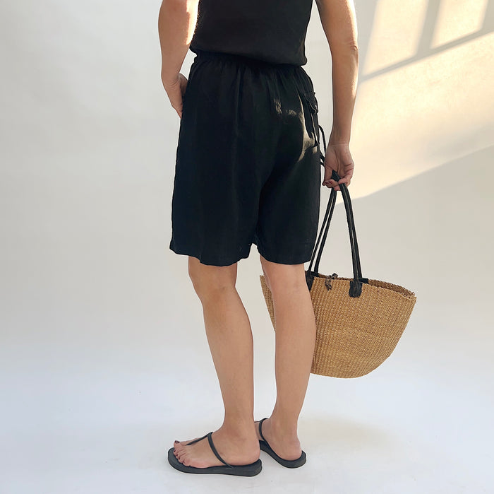Person wearing black shorts and holding a woven bag on a white background, viewed from the back