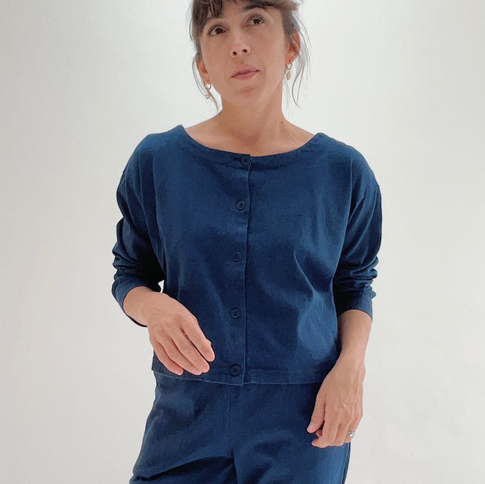 Close front view of model wearing Pacific Cotton nova long sleeve button front shirt, showing wide scoop neckline, five-button center placket, long sleeves, boxy cropped fit, and deep teal color