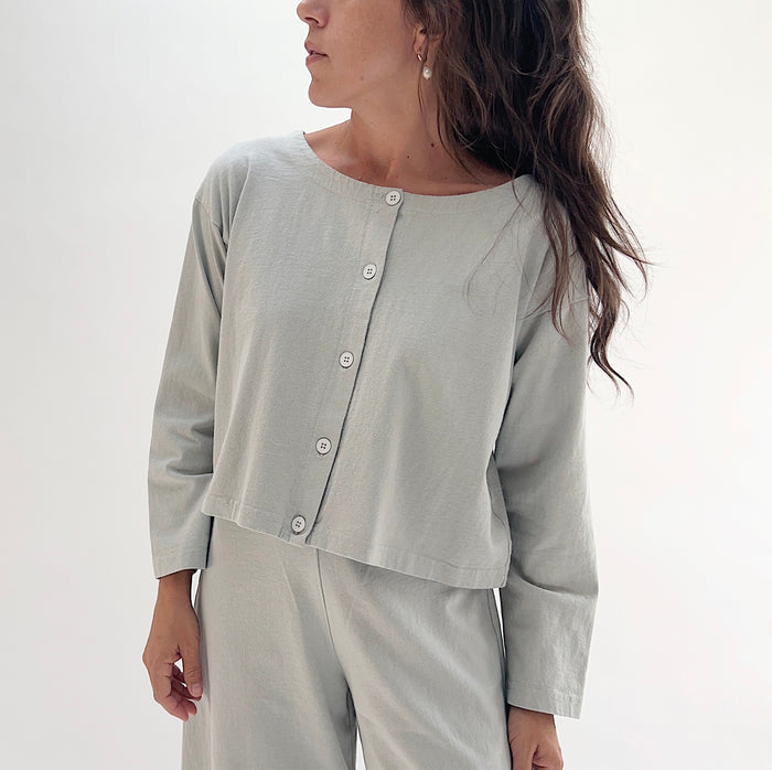 Close front view of model wearing Pacific Cotton orlaya long sleeve button front shirt, showing crew neckline, center button placket, long sleeves, and relaxed cropped boxy fit