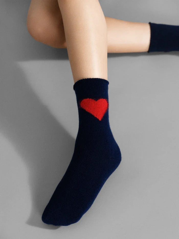 Love Cashmere Crew socks in Navy — navy cashmere crew with bold red heart motif and roll cuff, worn on a single foot against a grey background