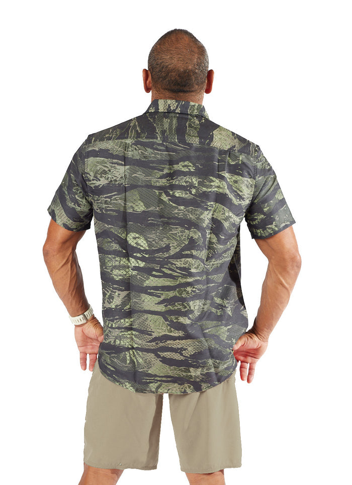 Back view of a male model wearing the Waihana Mens Tropicam Aloha Shirt in Tropicam Green camouflage print with khaki shorts on a white background.