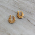 A pair of small chunky hexagonal gold hoop earrings on a marble surface.