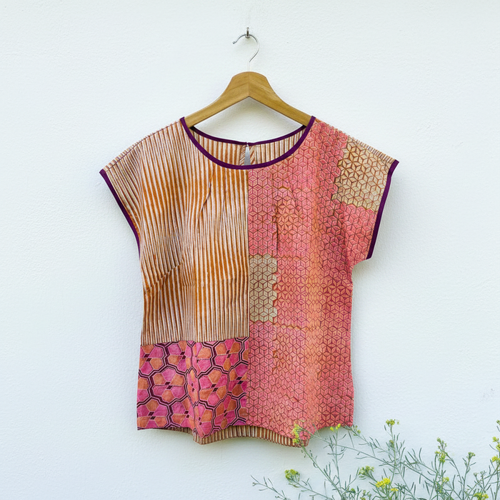 Colorful patterned red, orange and pink top on a wooden hanger against a white background