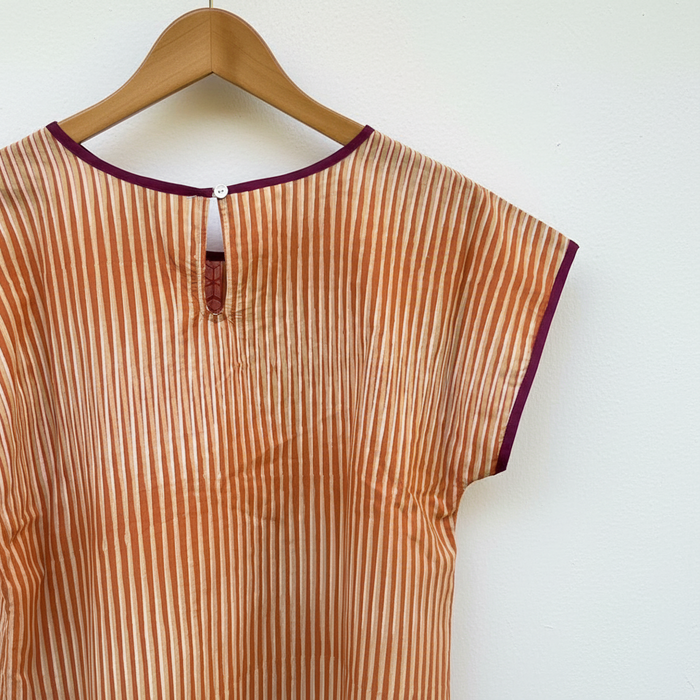 Striped shirt with purple trim on a wooden surface with a shell button closure
