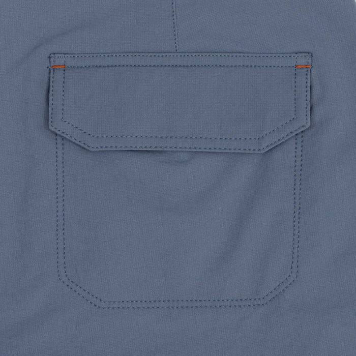 Close-up of the flap cargo pocket on the Waihana Offshore Blue Cruiser Shorts, showing double-stitched seams and orange bar-tack accent stitching against slate blue fabric.