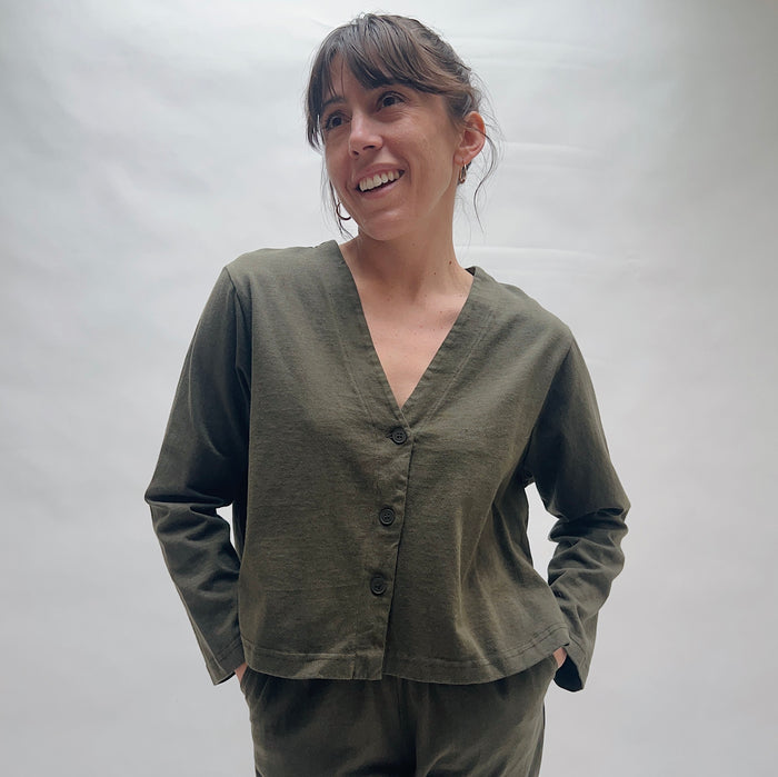 Woman wearing an olive green cardigan and pants against a plain background