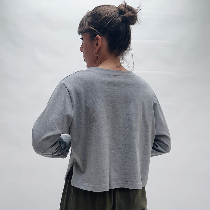 Person wearing a gray long-sleeve shirt against a white background, viewed from the back