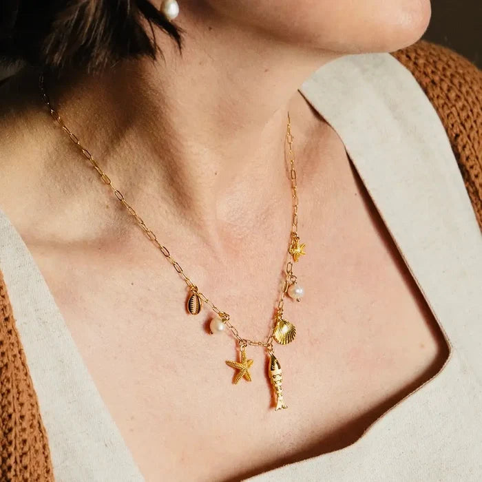 Gold necklace with shell and starfish charms worn by a person