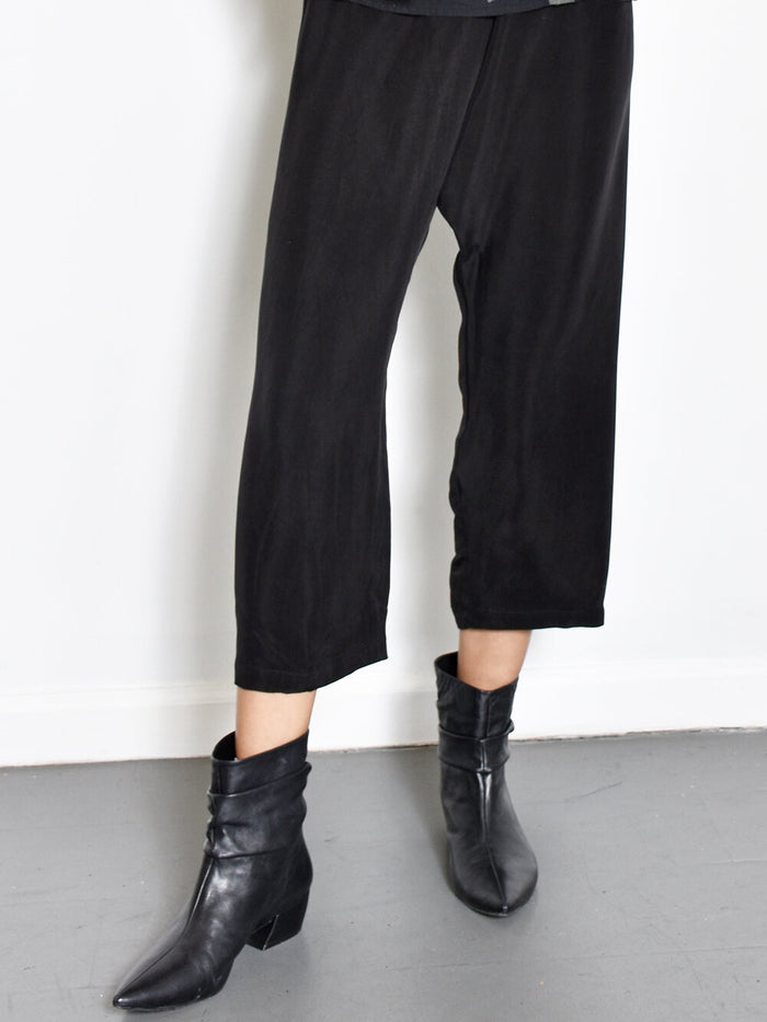A person wearing black cupro pants and black boots standing against a white background.