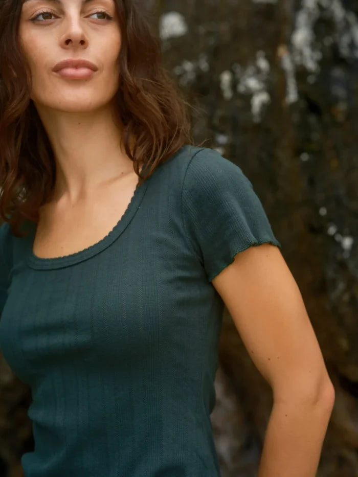 Close-up of female model wearing the Mollusk Surf Shop Pointelle Tee in Black Forest, showing scoop neck ruffled trim, short sleeve detail, and deep teal pointelle rib fabric texture