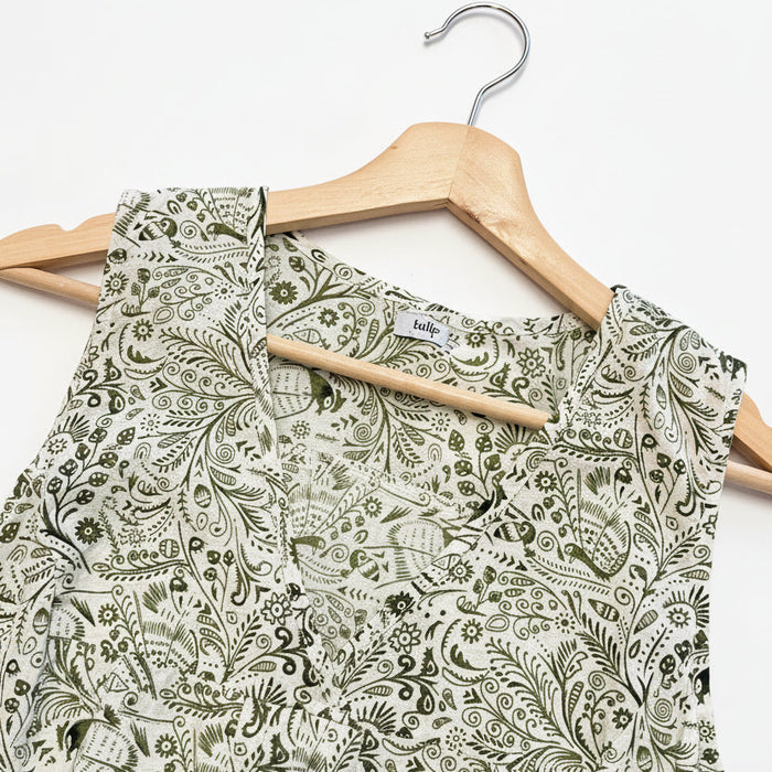 A sleeveless top with a dense olive green paisley and floral pattern on a white background, shown on a wooden hanger