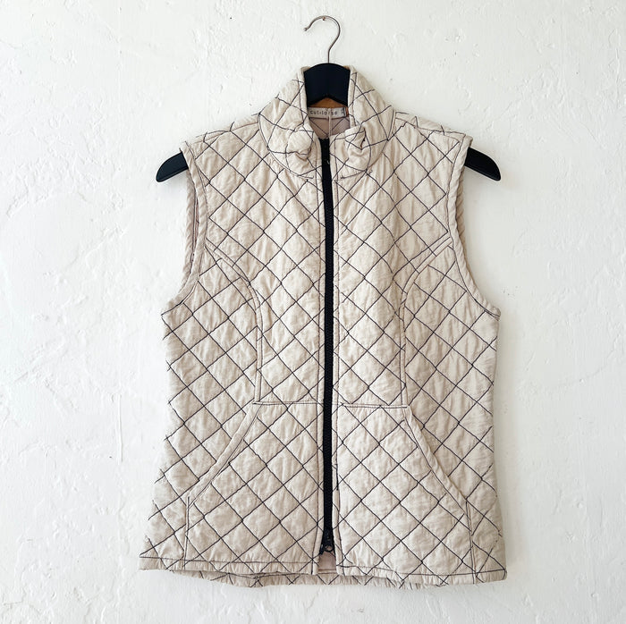 Cream-colored quilted vest with a diamond pattern on a hanger against a white wall